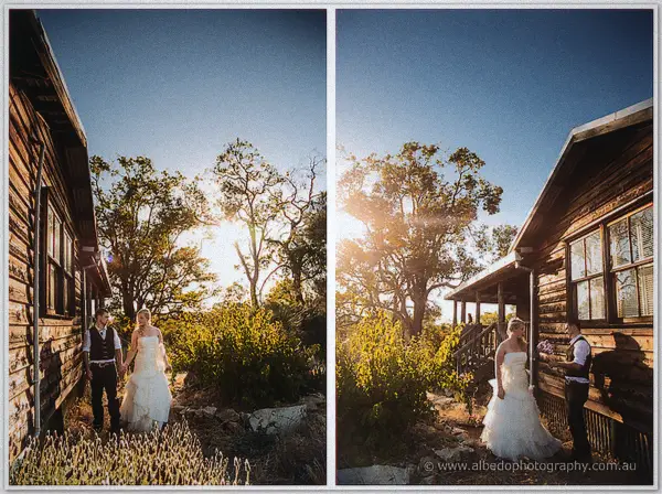 The couple stroll hand in hand past weathered slab huts as the sun bursts through trees