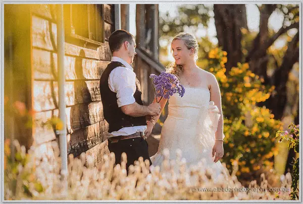 Gary offers Tash a bunch of dried purple flowers beside the timber hut in warm afternoon light