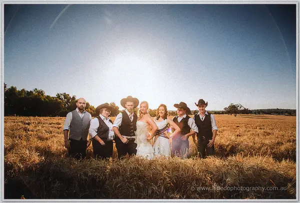 Bridesmaids and groomsmen line up shoulder to shoulder in the wheat, hats on, sun overhead