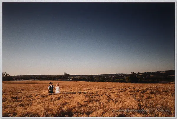 A distant view of the couple crossing the vast harvested field under moody dusk light