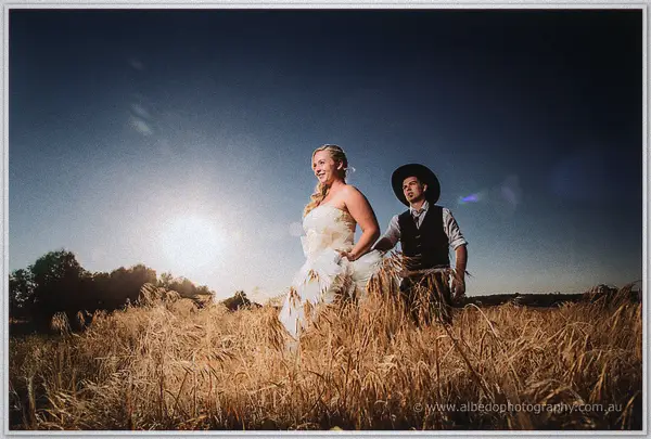 Tash laughs as she leads Gary through the tall oats, sun flaring low behind them