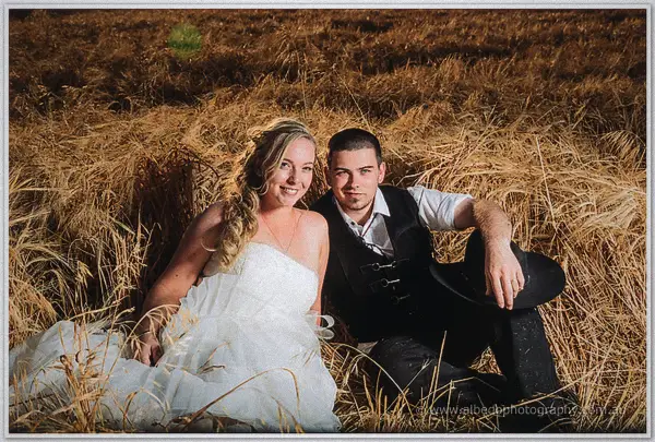 Tash and Gary sit nestled in golden straw, his hat in hand, warm light on their faces
