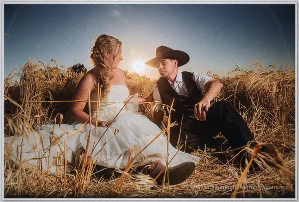 Tash and Gary sit close in the dry grass, sunlight flaring between them at dusk