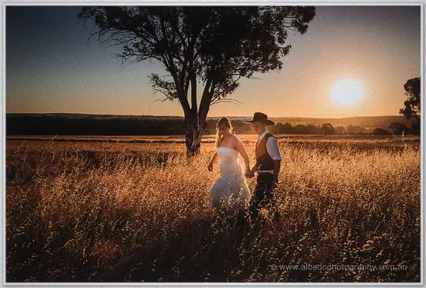 Tash and Gary wander hand in hand through backlit grass, the orange sun sinking low