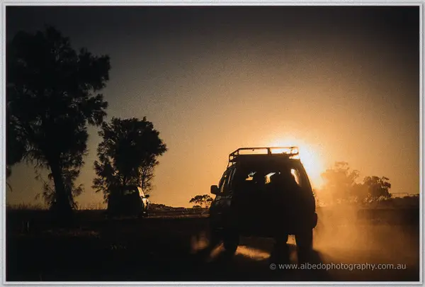 A four-wheel drive kicks up golden dust on the farm track as the sun drops behind trees