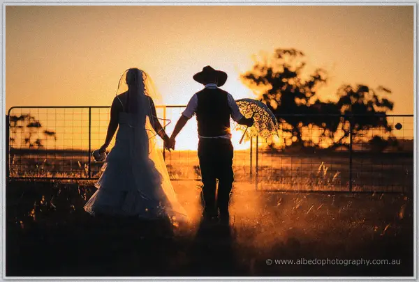 Silhouetted against the sunset, Tash leads Gary by the hand past a paddock fence