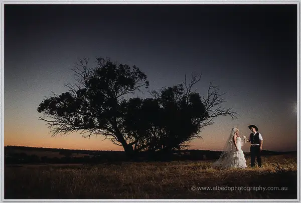 Tash and Gary stand small beneath a bare gum, torchlit against the last orange dusk