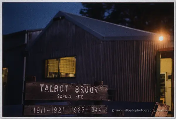 Twilight shot of the Talbot Brook school-site sign glowing beside the corrugated hall