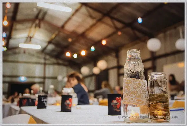 Lace-wrapped milk bottles dress the table under string lights in the rustic shed