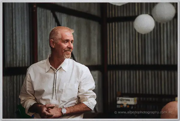 A grey-bearded guest in a bolo tie grins beneath the paper lanterns mid-reception