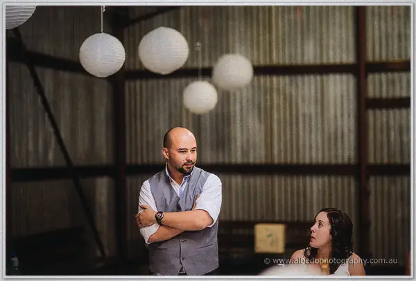A guest in a grey vest folds his arms and listens intently under the swag of lanterns