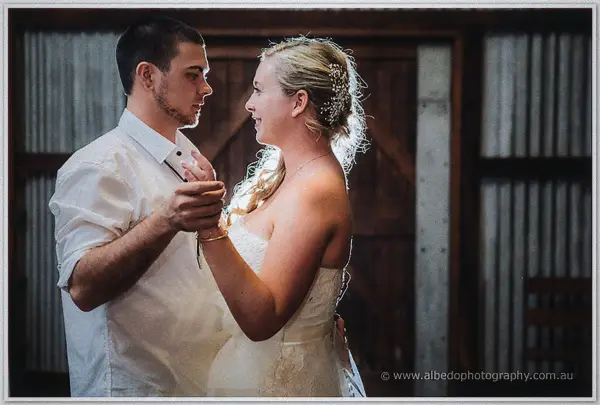 Tash and Gary sway through their first dance, sunlight rimming her hair against the shed walls