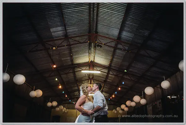 Tash and Gary kiss beneath the symmetrical corrugated roof strung with lanterns and fairy lights