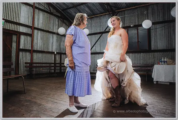 Tash swaps heels for brown boots as an older woman in lilac looks on in the lantern-lit shed