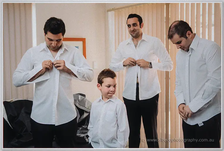 Craig and his groomsmen button their white shirts as a young page boy waits nearby