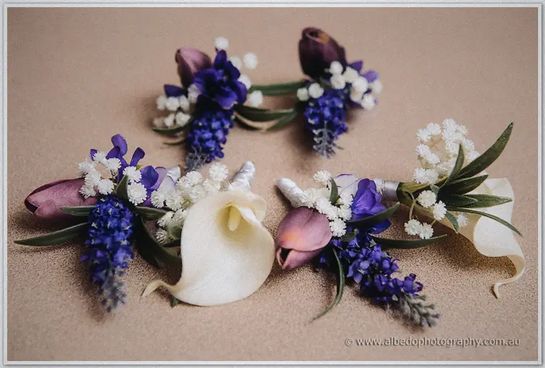 Purple muscari, plum tulips and white calla lily buttonholes laid out on a taupe carpet