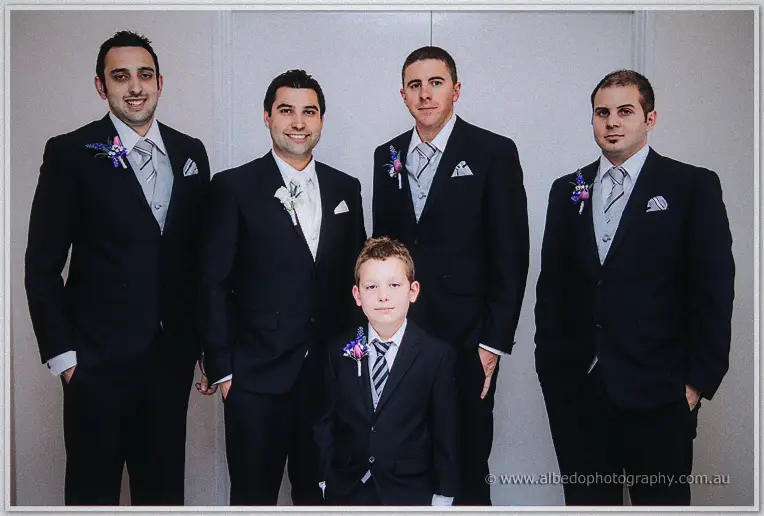 Craig and his groomsmen pose with the page boy in navy suits against a white wall