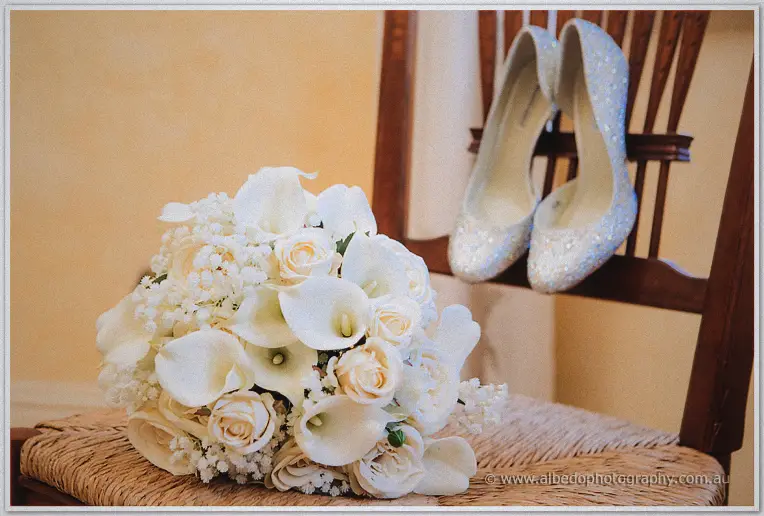 Amanda's white calla lily and rose bouquet rests on a rush-seated chair by her glittering heels