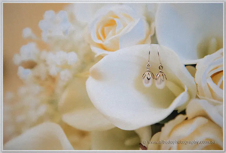 Pearl drop earrings nestled inside a white calla lily among cream roses