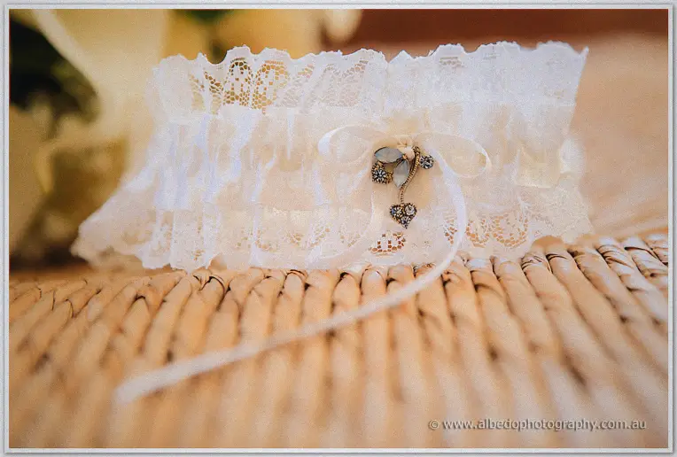 Lace bridal garter with a silver heart charm looped over a ribbon on a wicker chair