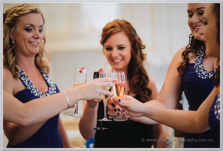 Bridesmaids in navy dresses clink champagne flutes garnished with raspberries