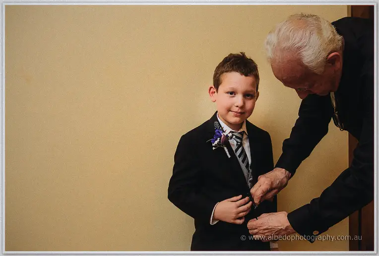 A grandfather buttoning the page boy's navy suit jacket before the ceremony