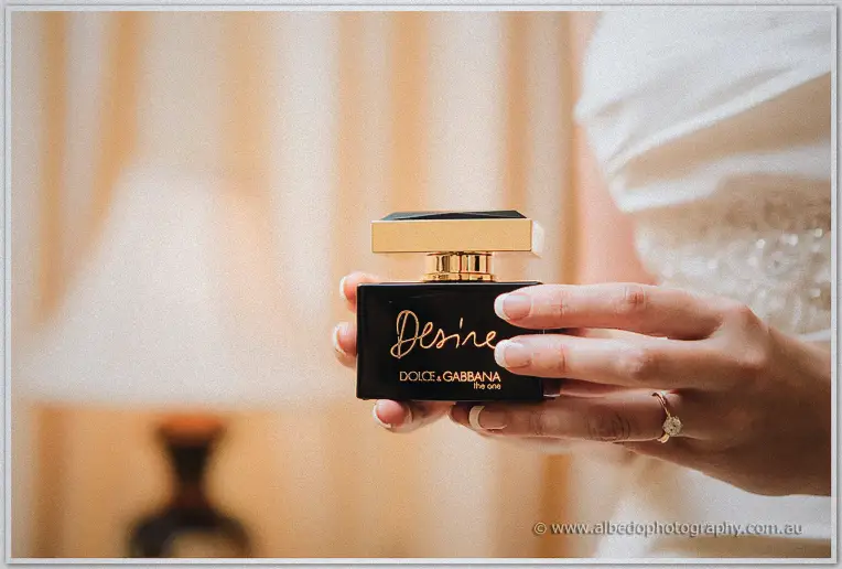 Amanda's hands holding a black and gold bottle of perfume by lamplight