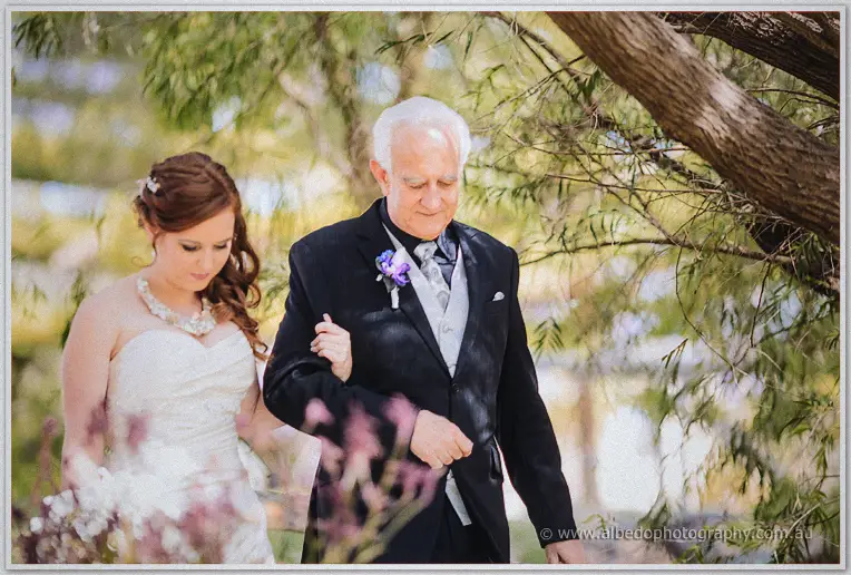 Amanda on her father's arm beneath weeping willow boughs before the ceremony
