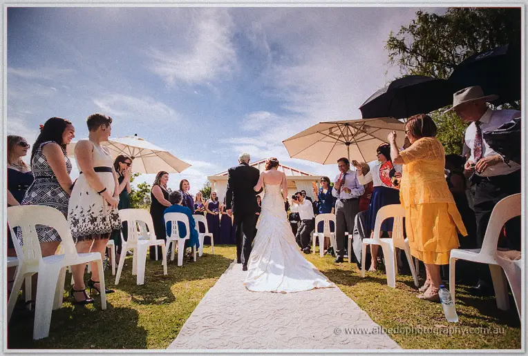 Amanda and her father walk the outdoor aisle between umbrella-shaded guests at Brookleigh