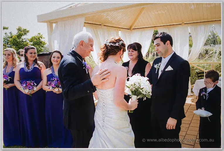 Amanda's father places her hand in Craig's beneath the cream ceremony pavilion