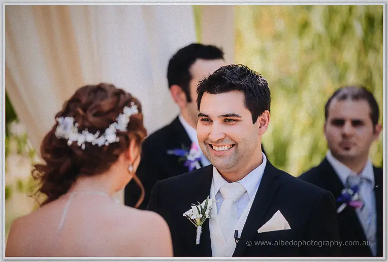 Craig beams at Amanda across the altar, groomsmen soft in the background