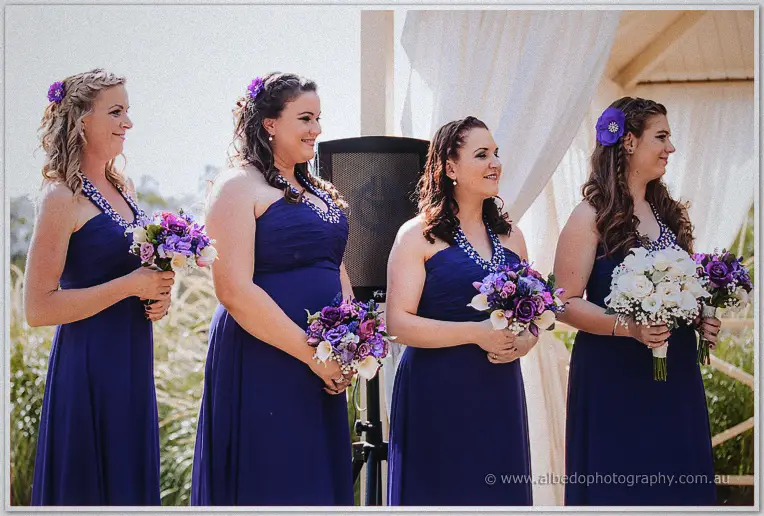 Four bridesmaids in navy halter gowns with purple bouquets lining the arbour
