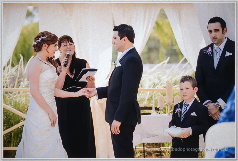 Craig taking Amanda's hands as the celebrant speaks under white drapery