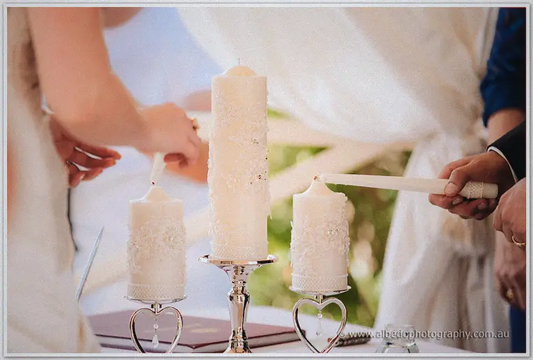 Close-up of the couple lighting white unity candles on silver heart stands during their outdoor ceremony