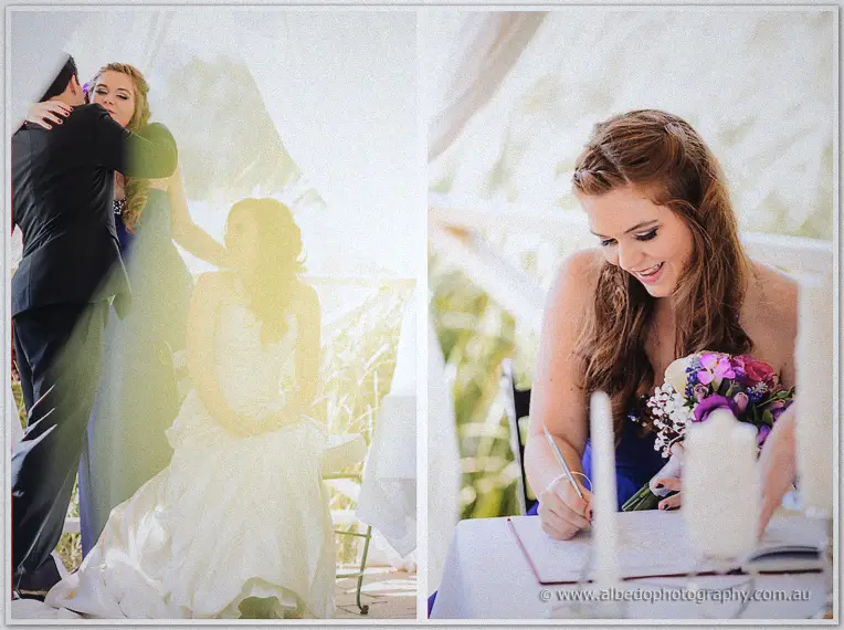 Bridesmaid in royal blue signs the marriage register while the seated couple embrace beneath sheer draping