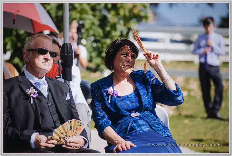 Wedding guests in blue fanning themselves against the summer heat on the Brookleigh Estate lawn