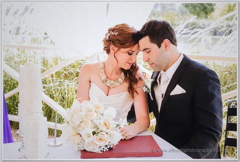 Amanda and Craig rest heads together over the register table beside her cream rose bouquet