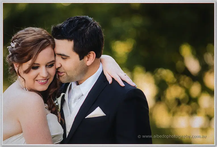 Craig nuzzles his smiling bride's temple among sun-dappled trees at Brookleigh Estate