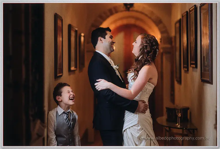 The laughing couple share a moment as the page boy cackles beside them in the hallway