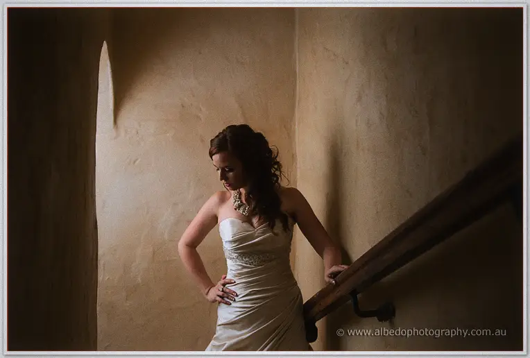 Amanda gazes down from the stair landing, soft window light on her strapless gown