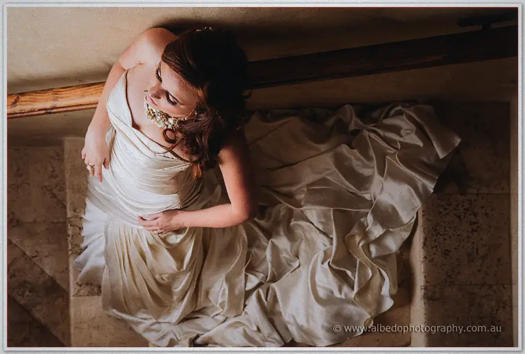 Amanda looks up at the camera from the stairs, her gown pooling in satin folds below