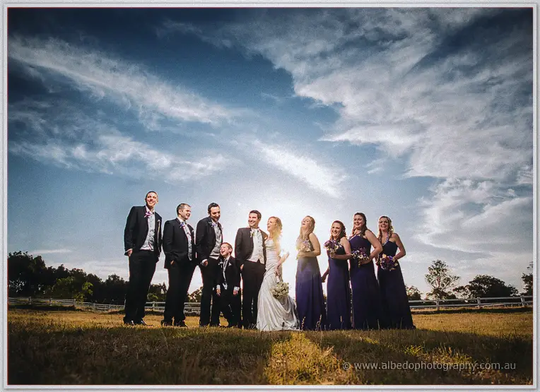 Bridesmaids and groomsmen laughing together under a glowing sunset sky at Brookleigh