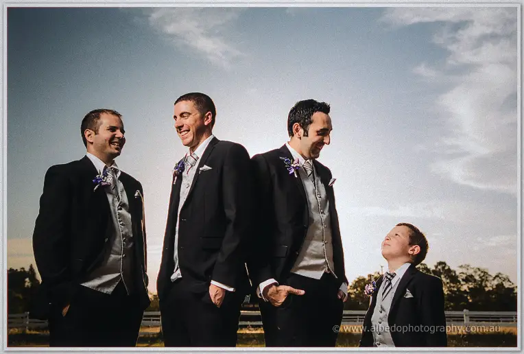 Three groomsmen and the small page boy share a laugh against the late-afternoon sky