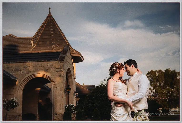 Amanda and Craig smile forehead to forehead in soft evening light beside the estate's stone turret