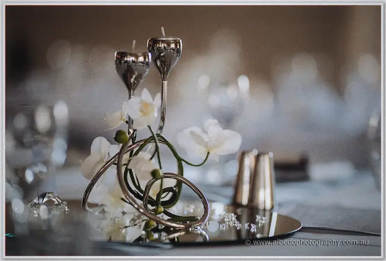 A close-up of white orchids wound through silver candlesticks mirrors on a polished reception table