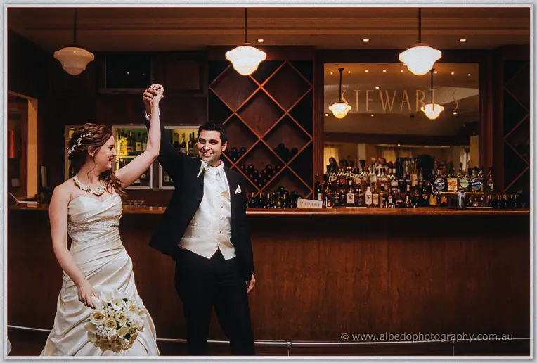 Craig twirls a beaming Amanda in front of the timber bar beneath glowing pendant lights at the reception