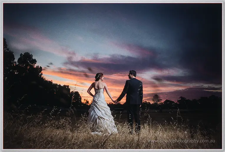 Amanda and Craig hold hands and gaze at the horizon as the last sunset colour deepens over the paddock