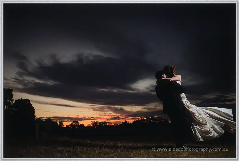 Craig sweeps Amanda into a dip, her train billowing, beneath brooding indigo clouds and a fading horizon