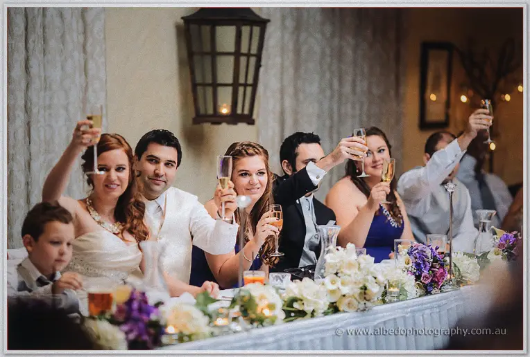 Craig in a cream waistcoat raises his champagne as the wedding party toasts down the festooned bridal table