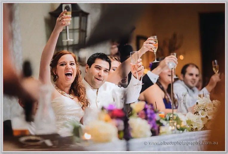 Amanda cheers with her champagne arm flung high as Craig and the wedding party raise their flutes in toast